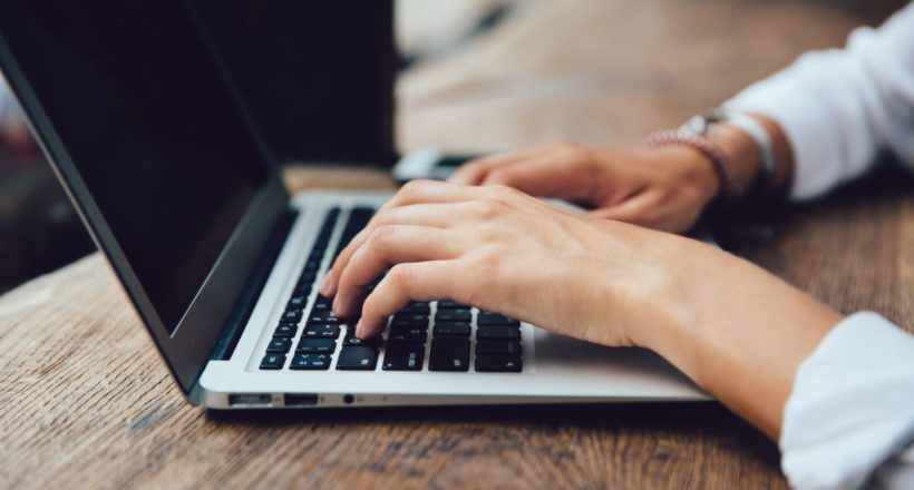 Close-up view of female hands typing on keyboard of laptop